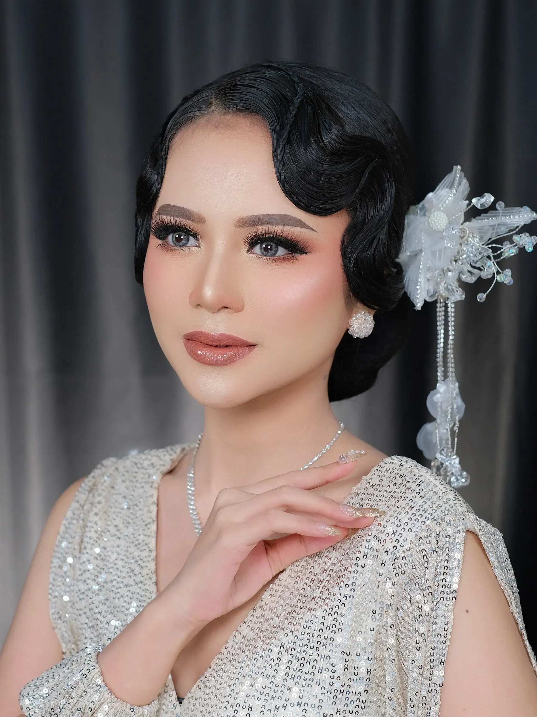 Riasan glam dengan hairdo gelombang klasik, hiasan rambut perak, dan busana berpayet perak
