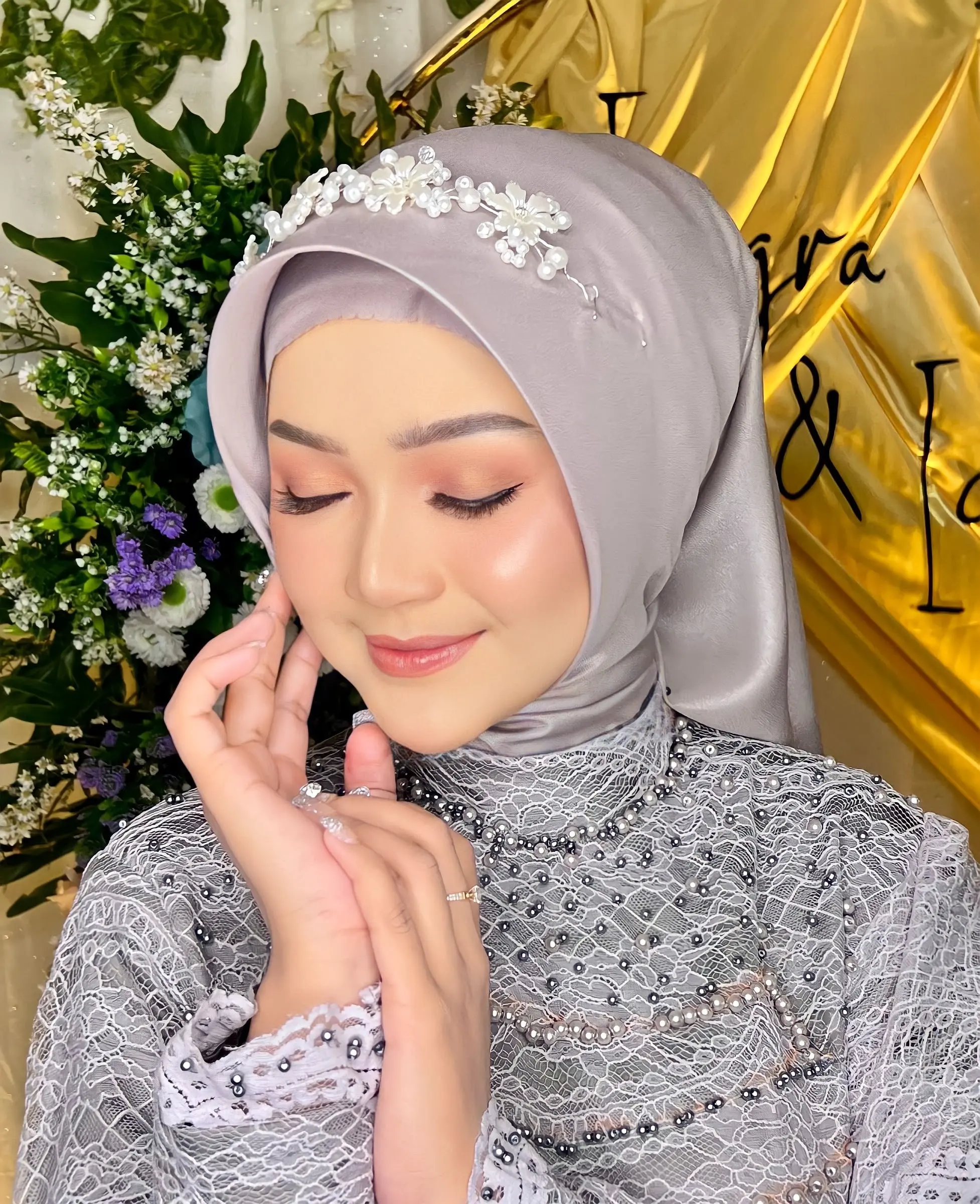 Riasan soft glam berhijab abu-abu dengan hiasan kepala mutiara dan kebaya abu berpayet