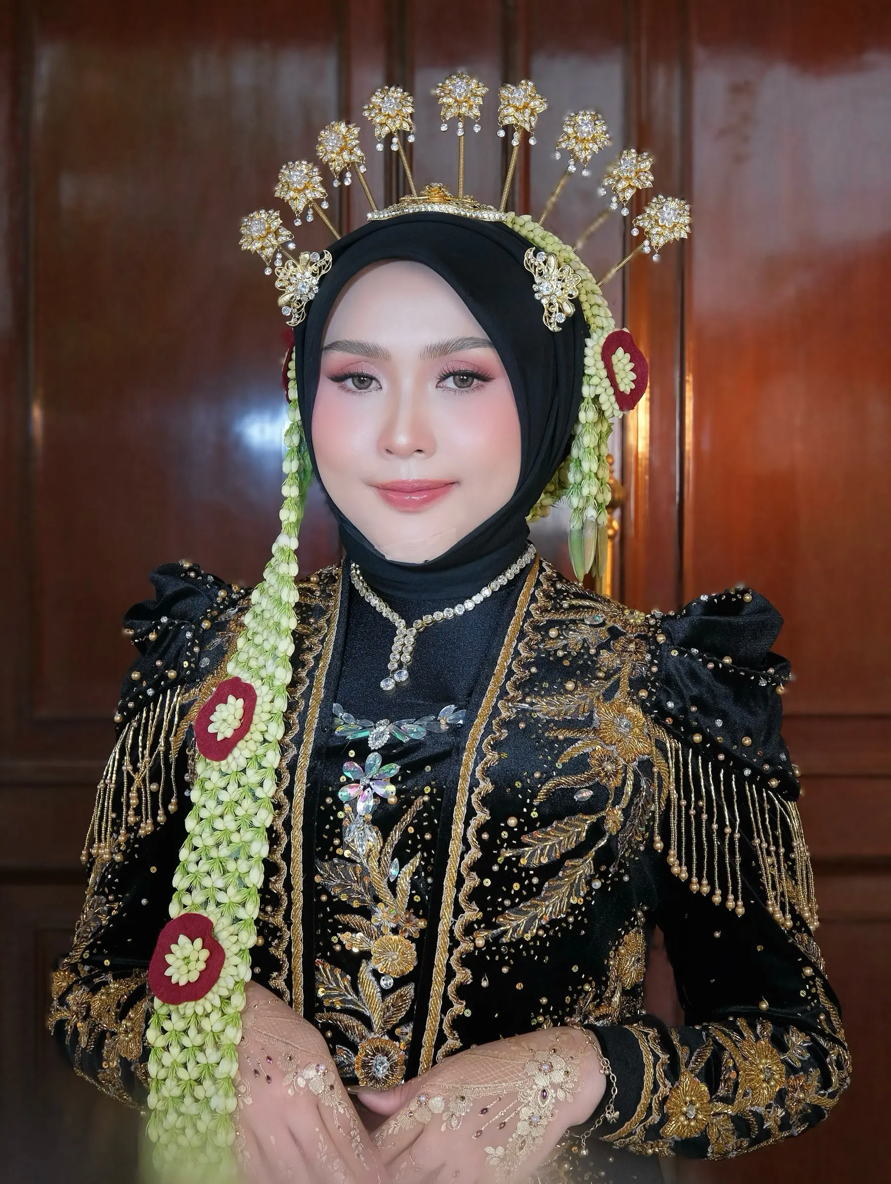Pengantin berhijab hitam dengan mahkota emas dan kebaya beludru hitam berpayet emas