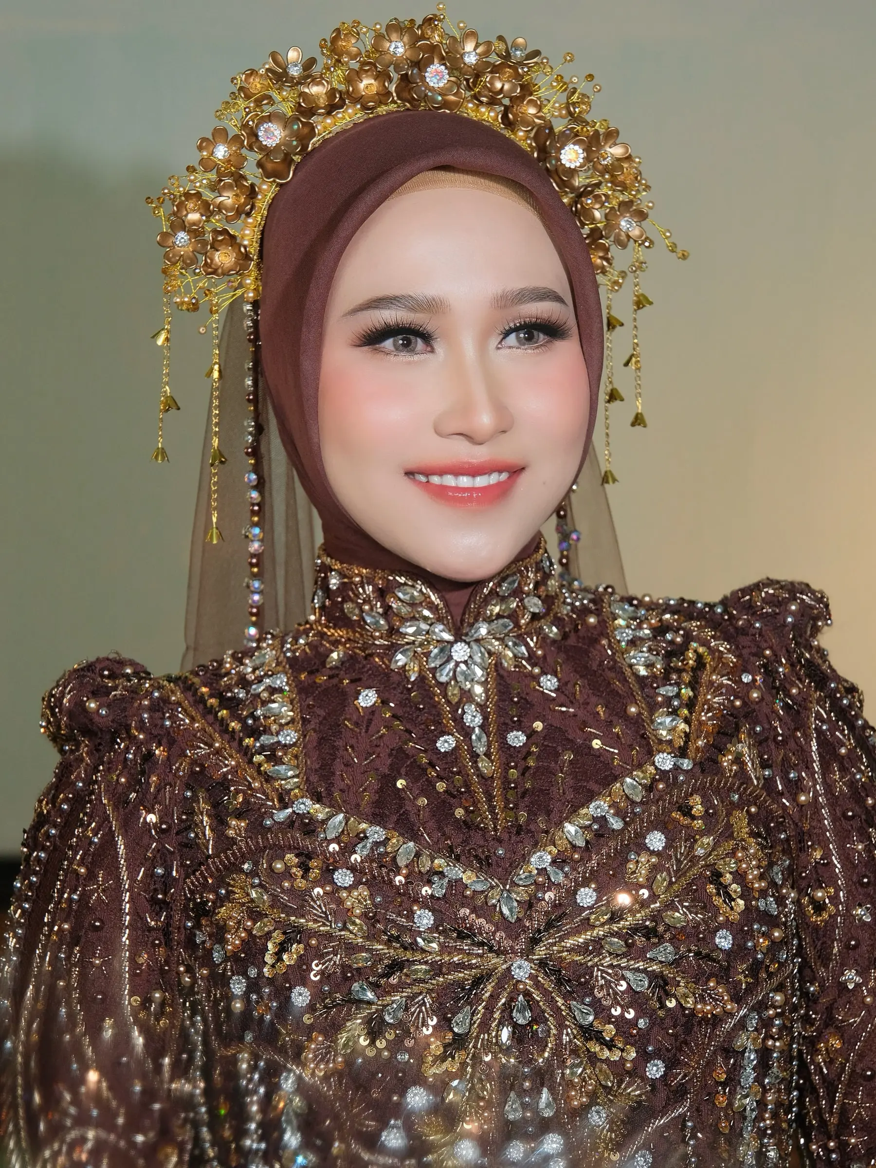 Riasan ngunduh mantu: pengantin berhijab cokelat dengan mahkota emas dan kebaya cokelat berpayet