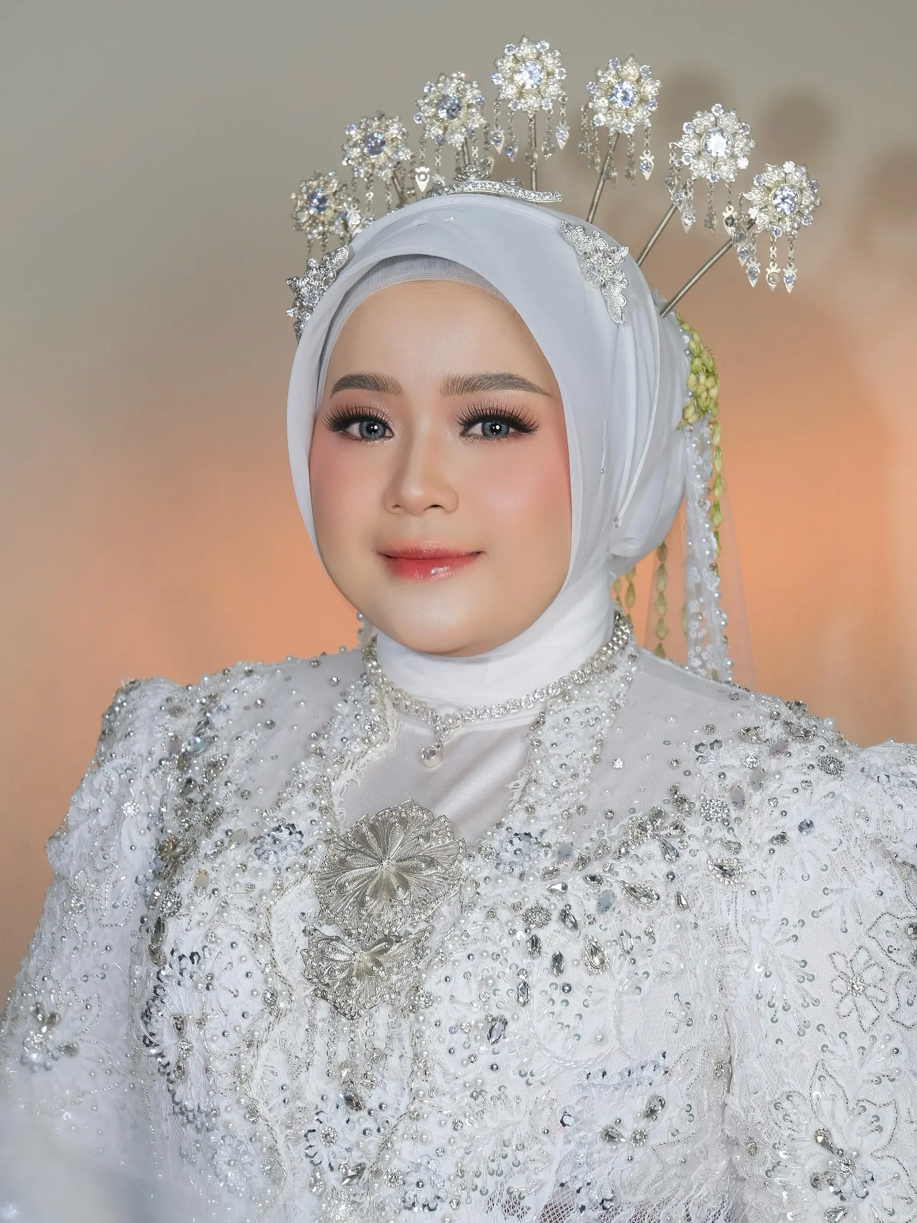 Pengantin berhijab putih dengan mahkota perak dan kebaya putih berpayet