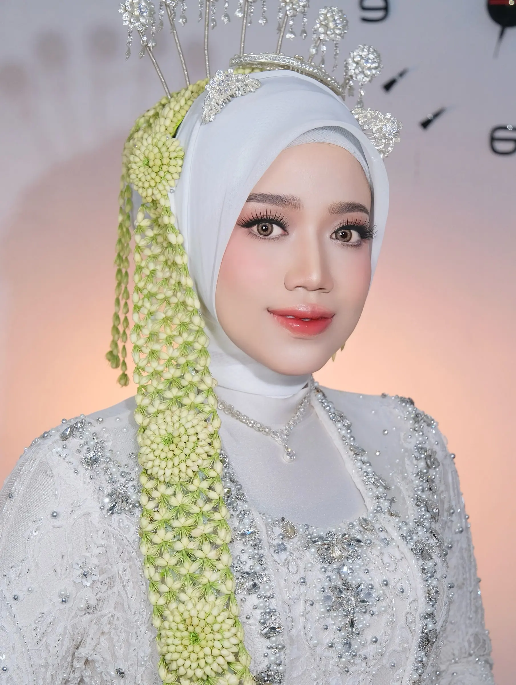 Pengantin berhijab putih dengan siger perak, ronce melati, dan kebaya putih penuh payet