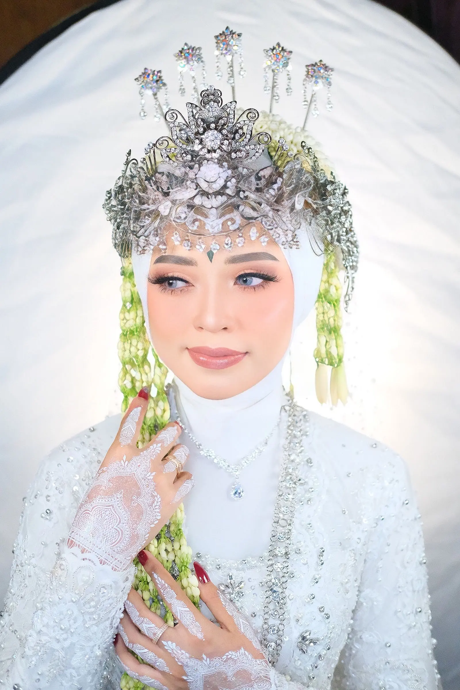 Pengantin berhijab putih dengan siger perak dan henna putih di tangan