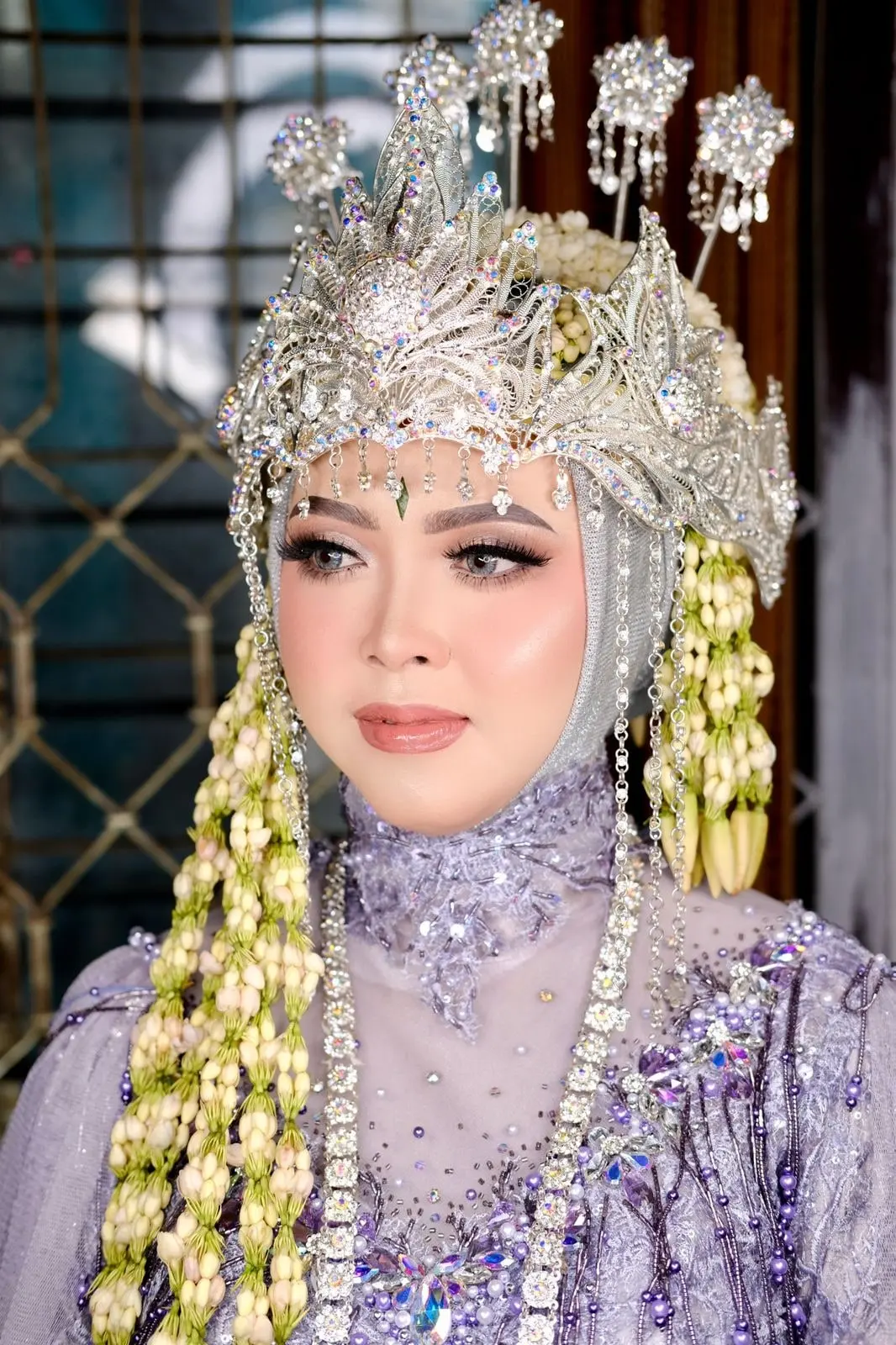 Pengantin berhijab dengan siger perak, ronce melati, dan kebaya lilac