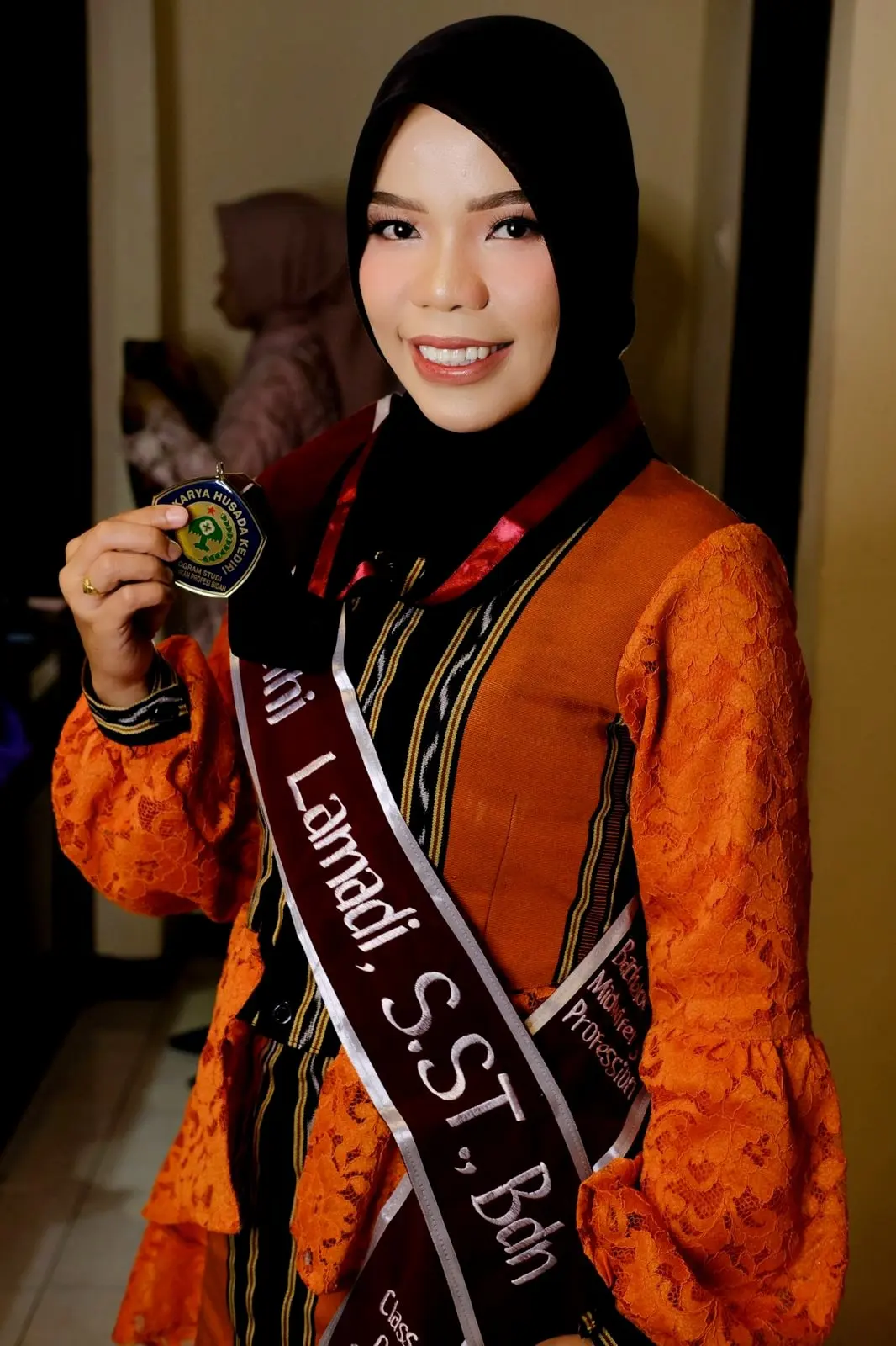 Riasan wisuda: wisudawati berhijab hitam memakai kebaya jingga dan selempang